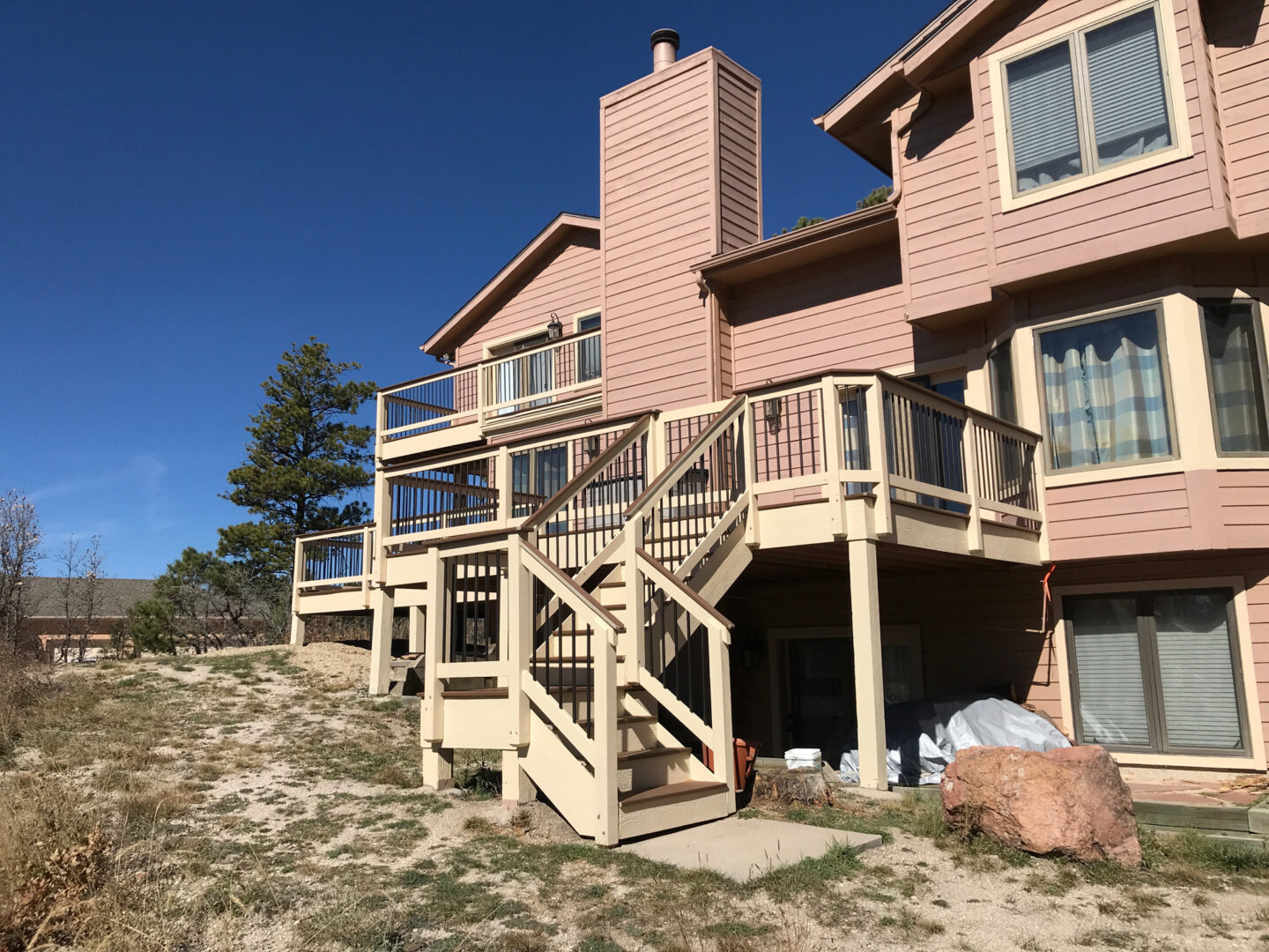 A wooden deck with stairs attached to a two-story house in a dry, grassy area.