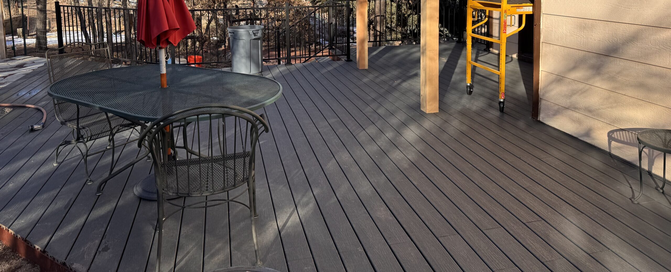 Sunny outdoor deck with metal table, chairs, and a red umbrella.